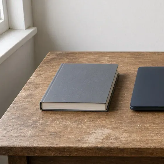 A closed gray catalog on a wood desk, with the corner of a closed laptop at the right edge.