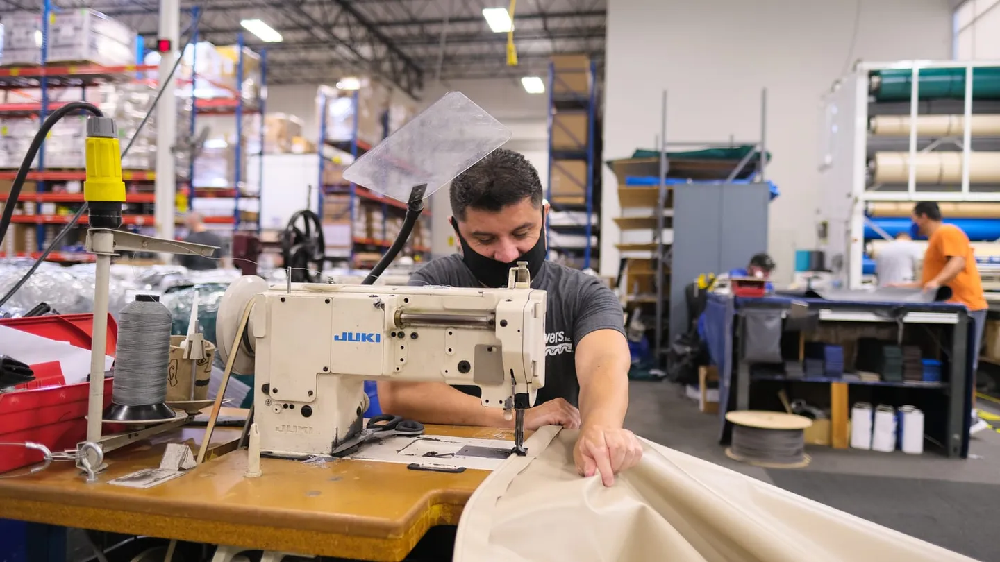 Worker at an industrial sewing station on a factory floor, the kind of site visit that comes after cheap documentary checks.